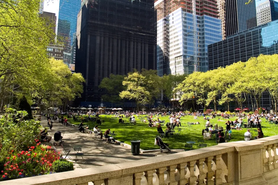 Green lawn in city park full of people sitting on lawn chairs with urban high-rises in background.